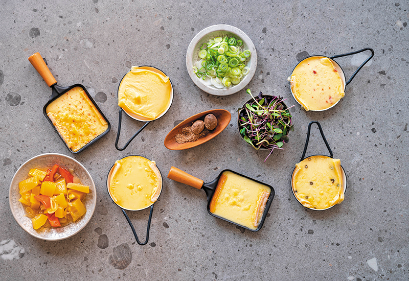 Ein Arrangement mit Raclette Pfannen, Salaten, Gewürzen, und Gemüsen