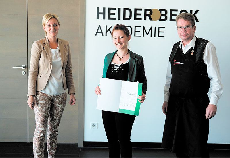 Bild von der Diplom Übergabe an Nadja Thoma mit ihrem Zeugnis zum Diplom Käsesommelier. Rechts Lehrerin Christina Nussbaumer, links Hans Peter Chiste.