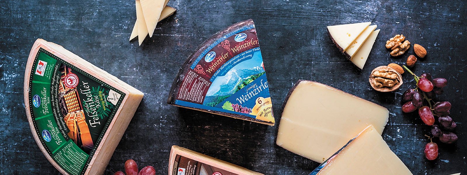 Eine Käsesplatte mit verschiedenen Käsestücken der Tirol Milch auf dunkelblauem Hintergrund