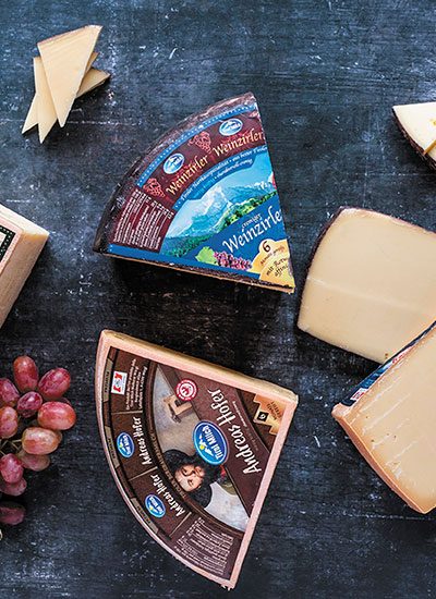 Eine Käsesplatte mit verschiedenen Käsestücken der Tirol Milch auf dunkelblauem Hintergrund