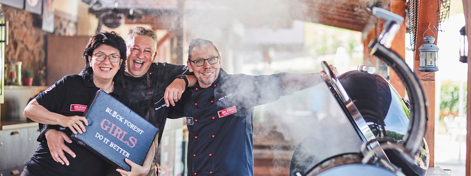 Das Grillteam von Forum Culinaire mit Maria Bruder, Gehard Volk und Heiner Haseidl präsentiert sich vor einem brennenden Grill
