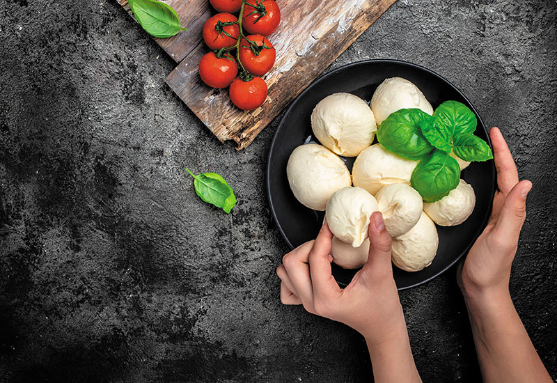 Ein Teller mit Büffelmozzarella wird mit Tomaten und frischem Basilikum angerichtet