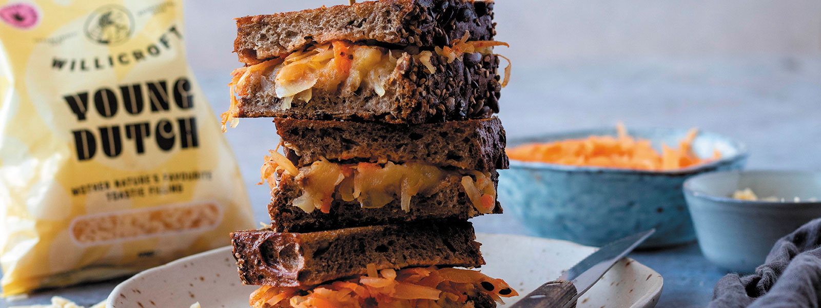 Ein Käsetoastsandwich mit blauen Töpfen im Hintergrund und einer Packung Young Dutsch, einem veganen Käse