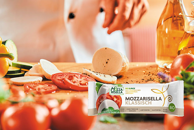 Ein Tisch mit einer aufgeschnittenen Bio Mozzarella, davor die Packung ungeöffnet und daneben Tomaten