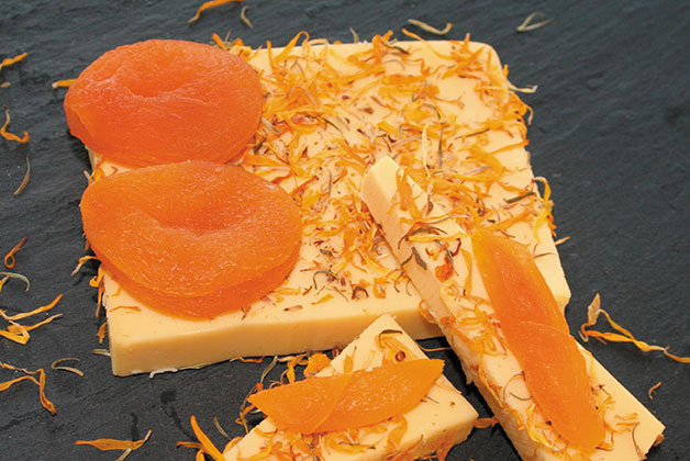 Auf einer Schieferplatte liegt der vegane Käse angeschnitten und mit Kräutern bestäubt