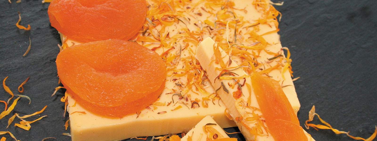 Auf einer Schieferplatte liegt der vegane Käse angeschnitten und mit Kräutern bestäubt