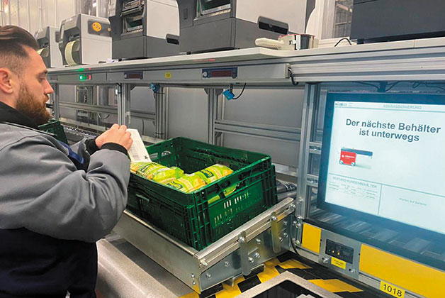 Ein Mitarbeiter etikettiert eine Kiste mit Käse, die er gerade am Autostore Port kommissioniert hat.