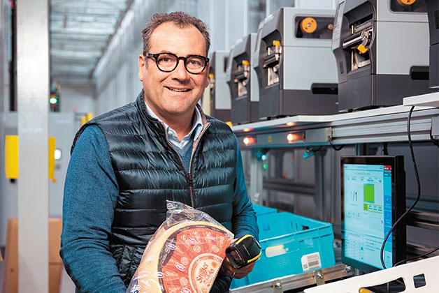 Peter Steding steht am Autostore und kommissioniert einen halben Laib Stilfser Käse