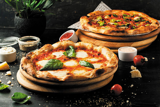 Zwei Teller mit zwei aufgebackenen Pizzen, daneben Gewürze und Kräuter